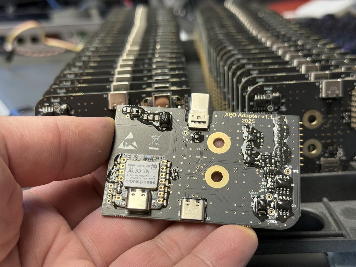 XPO USB-C PD adapter board held in hand, production units behind